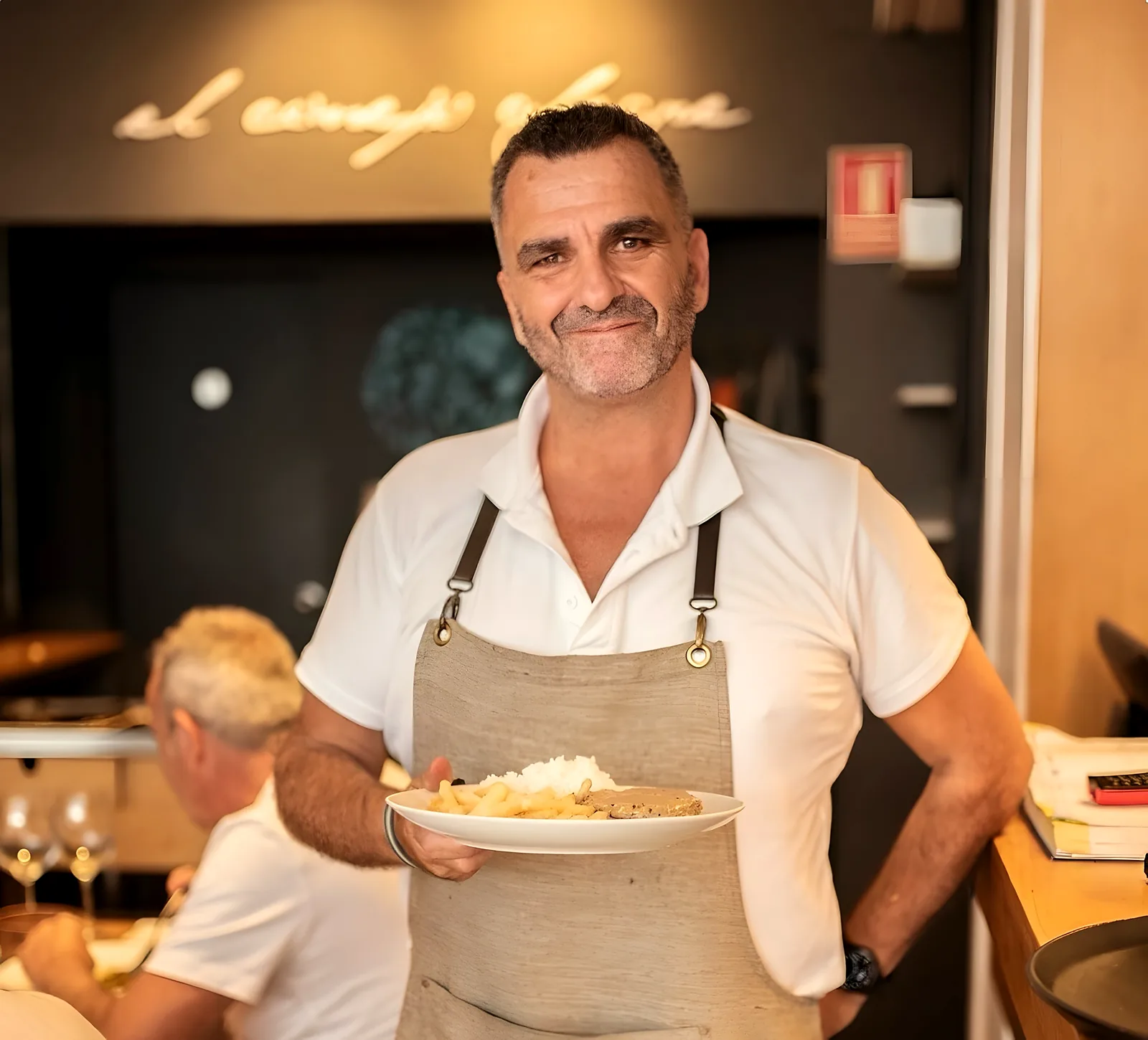 El anfitrión de la casa, con delantal de lino, sonríe con un plato en la mano en la sala