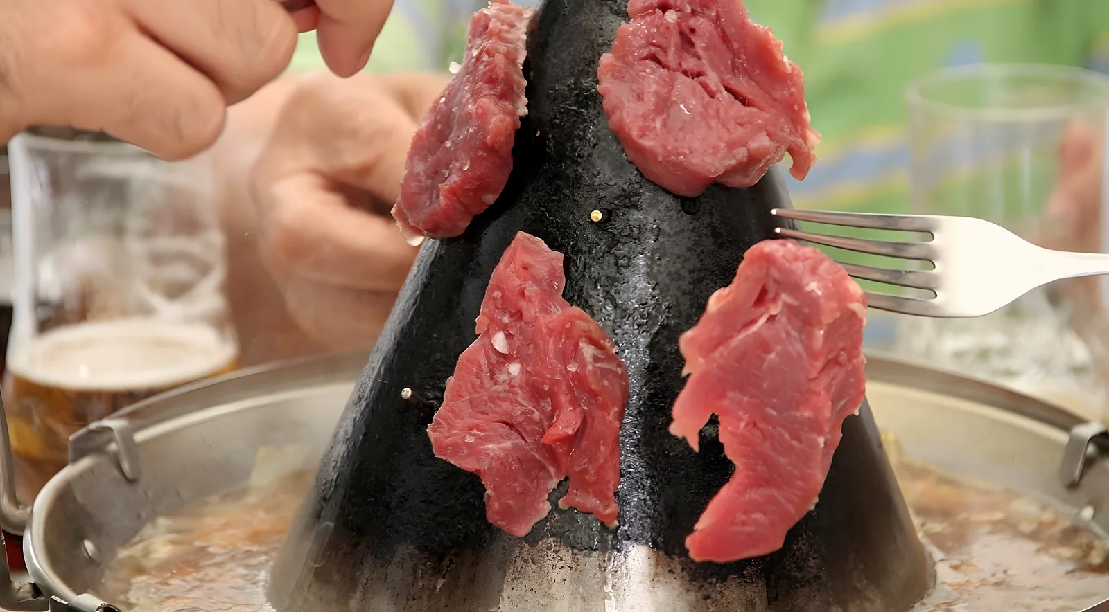 Láminas de carne cruda colocadas sobre el sombrero de hierro caliente