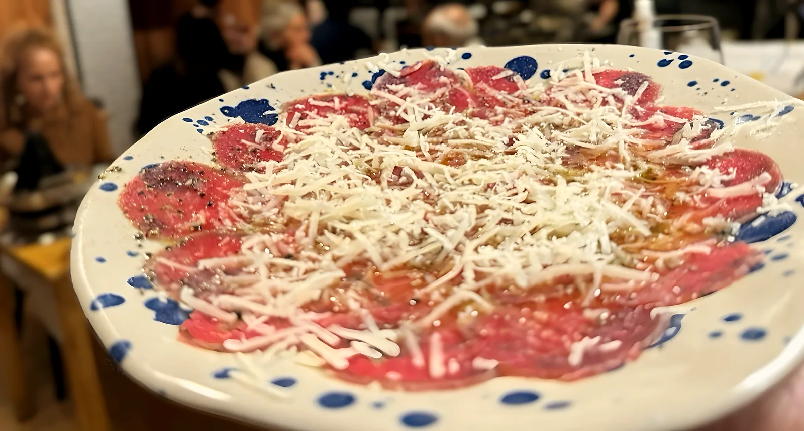 Carpaccio con queso rallado en plato de cerámica moteada de azul, en la sala