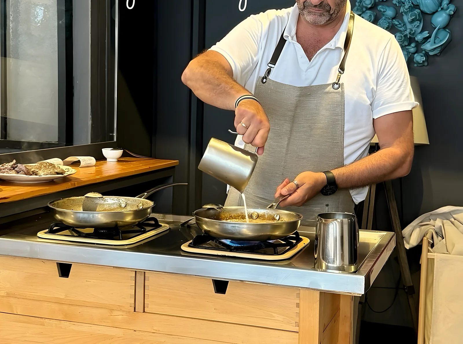 El cocinero vierte la salsa en la sartén, en el pase abierto a la sala